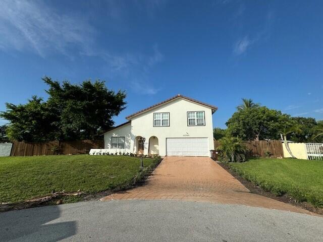 6785 Escondida Dr, Lake Clarke Shores, FL 33406 - traditional-style home featuring fence, an attached garage, stucco siding, a front lawn, and decorative driveway