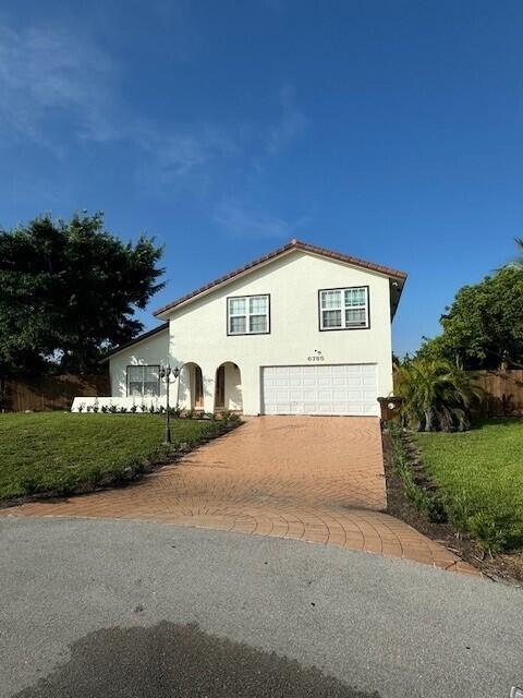 6785 Escondida Dr, Lake Clarke Shores, FL 33406 - view of front of house with a front yard, decorative driveway, stucco siding, and a garage