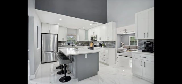 6785 Escondida Dr, Lake Clarke Shores, FL 33406 - kitchen with a breakfast bar area, decorative backsplash, light countertops, a kitchen island, and appliances with stainless steel finishes