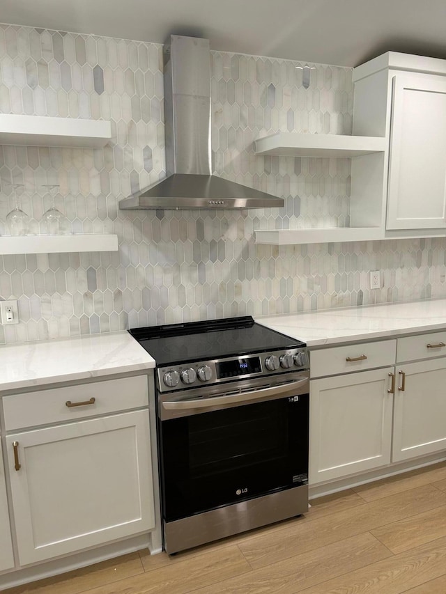 kitchen with wall chimney exhaust hood, white cabinetry, light hardwood / wood-style floors, light stone counters, and electric range