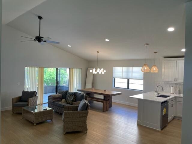 living room with lofted ceiling, sink, ceiling fan with notable chandelier, and light hardwood / wood-style floors