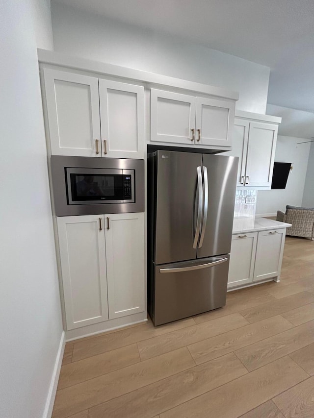 kitchen with decorative backsplash, white cabinets, stainless steel appliances, and light wood-type flooring