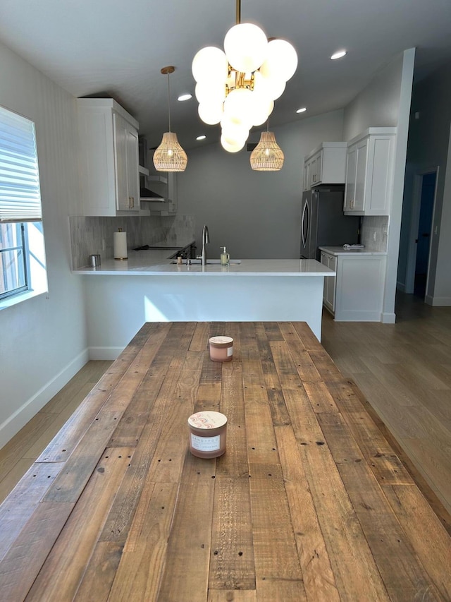 kitchen featuring tasteful backsplash, pendant lighting, kitchen peninsula, sink, and white cabinetry