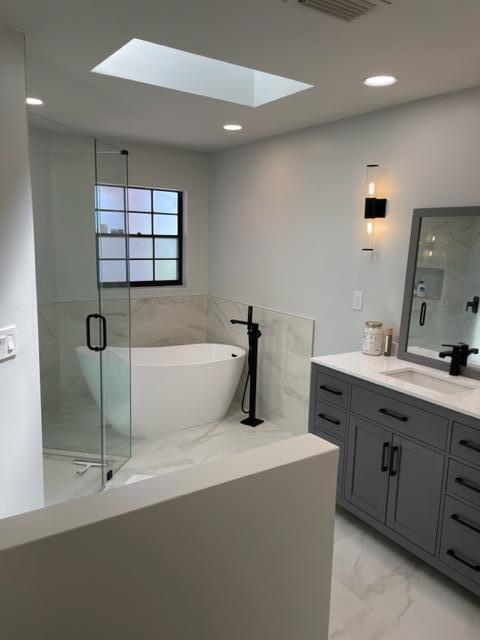 bathroom with plus walk in shower, a skylight, and vanity