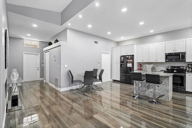 kitchen featuring a kitchen breakfast bar, backsplash, wood-type flooring, white cabinetry, and appliances with stainless steel finishes