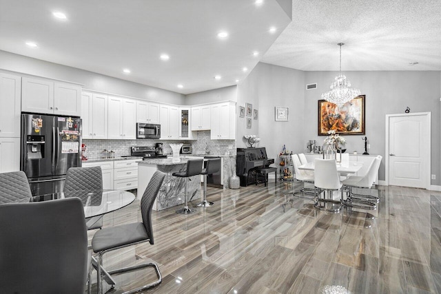 interior space with appliances with stainless steel finishes, light hardwood / wood-style flooring, a textured ceiling, white cabinets, and a breakfast bar area