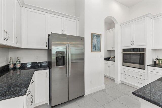 kitchen with appliances with stainless steel finishes, light tile patterned flooring, white cabinets, and dark stone counters