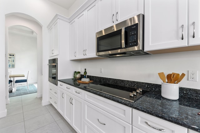 kitchen with light tile patterned floors, stainless steel appliances, dark stone countertops, and white cabinets