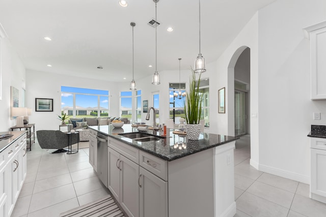 kitchen featuring dark stone counters, sink, light tile patterned floors, and an island with sink