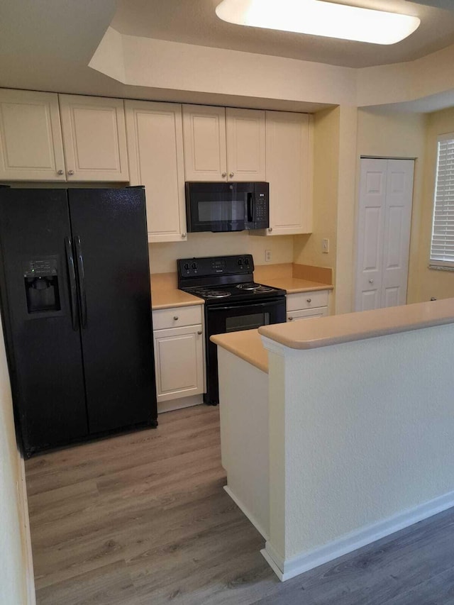 kitchen with light wood-type flooring, white cabinetry, and black appliances