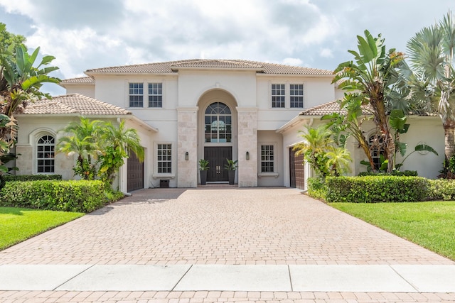 mediterranean / spanish house featuring decorative driveway, a tile roof, an attached garage, and stucco siding