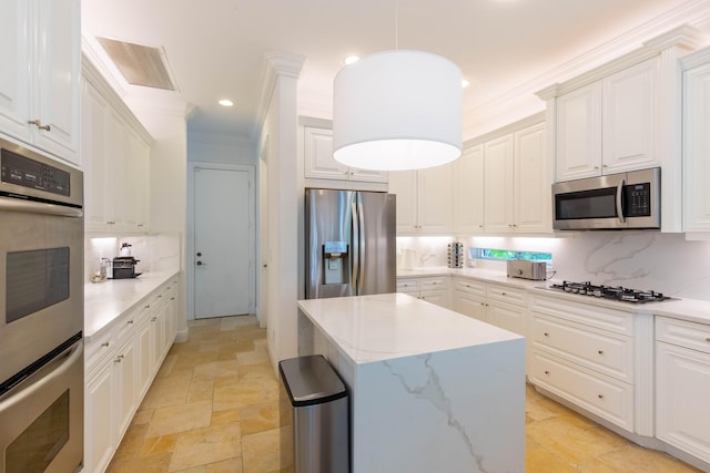 kitchen with crown molding, stone tile floors, backsplash, appliances with stainless steel finishes, and a kitchen island