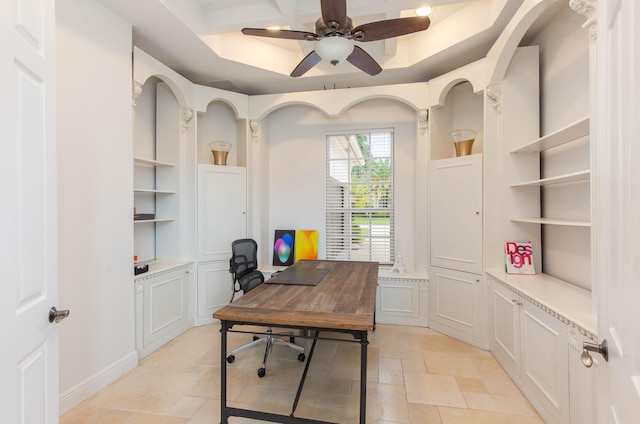 home office with a ceiling fan, stone finish flooring, a raised ceiling, and built in shelves