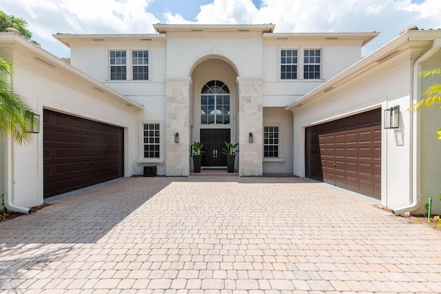 mediterranean / spanish house with a garage, stone siding, decorative driveway, and stucco siding