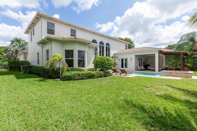 rear view of property with stucco siding, a pool with connected hot tub, a lawn, and a patio