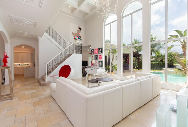 living room with arched walkways, coffered ceiling, an inviting chandelier, a high ceiling, and stone tile flooring