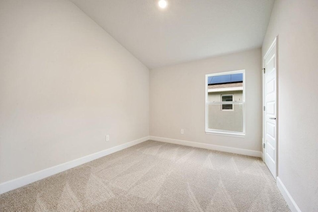 carpeted spare room featuring vaulted ceiling