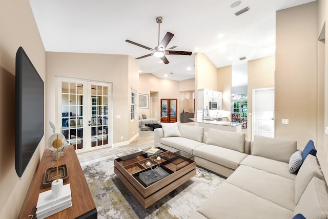 living room with ceiling fan, light hardwood / wood-style flooring, high vaulted ceiling, and french doors