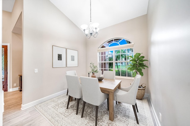 dining room with light wood-type flooring, high vaulted ceiling, and an inviting chandelier