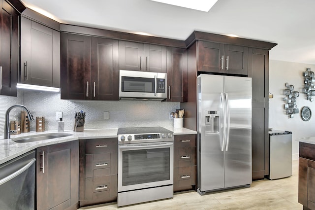 kitchen featuring appliances with stainless steel finishes, decorative backsplash, dark brown cabinetry, sink, and light wood-type flooring