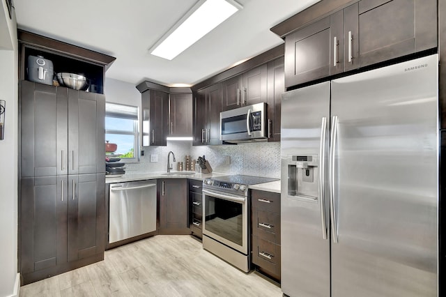 kitchen with appliances with stainless steel finishes, light hardwood / wood-style flooring, decorative backsplash, dark brown cabinets, and sink