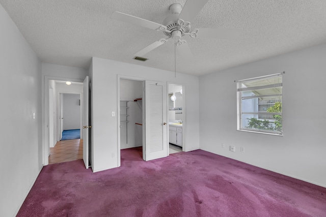 unfurnished bedroom featuring ceiling fan, a textured ceiling, a spacious closet, carpet floors, and ensuite bath