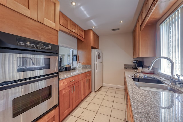 kitchen featuring white refrigerator, light tile patterned flooring, sink, stainless steel double oven, and light stone countertops