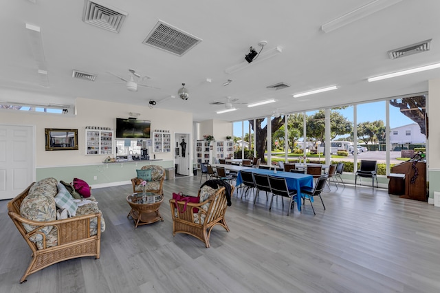 living room featuring light wood-type flooring, ceiling fan, and a wall of windows