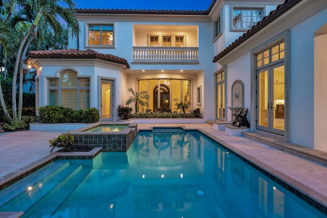 back of house with a patio area, french doors, a balcony, a tile roof, and stucco siding