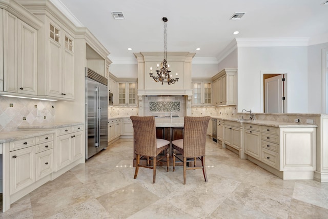 kitchen with an inviting chandelier, tasteful backsplash, stainless steel appliances, cream cabinetry, and light stone counters