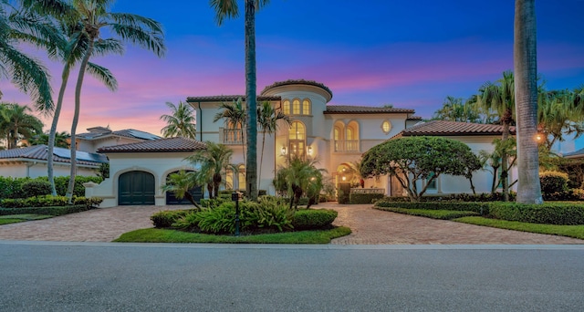 mediterranean / spanish-style home with a balcony, a tile roof, a garage, stucco siding, and decorative driveway
