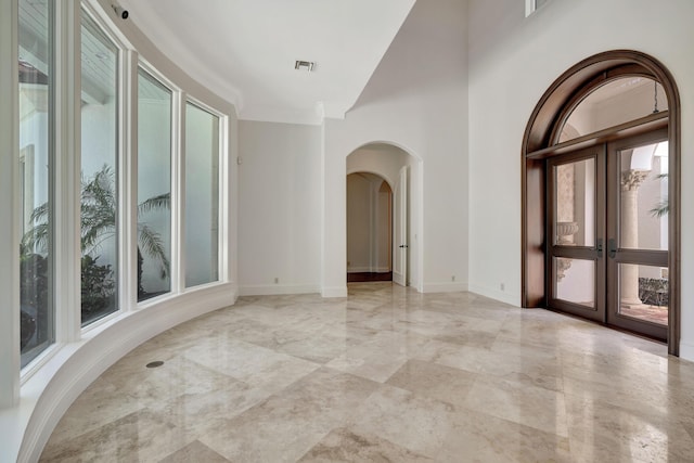 unfurnished room with arched walkways, a healthy amount of sunlight, french doors, and visible vents