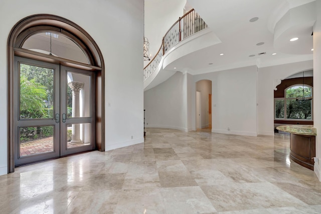 entrance foyer with a towering ceiling, a wealth of natural light, arched walkways, and french doors