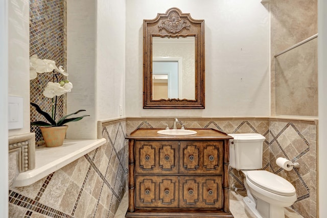 half bathroom with toilet, tile walls, wainscoting, and vanity