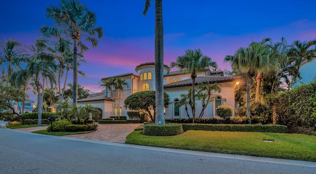 mediterranean / spanish home with a tiled roof, decorative driveway, stucco siding, and a lawn