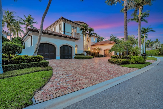 mediterranean / spanish home with a balcony, a tile roof, a garage, stucco siding, and decorative driveway