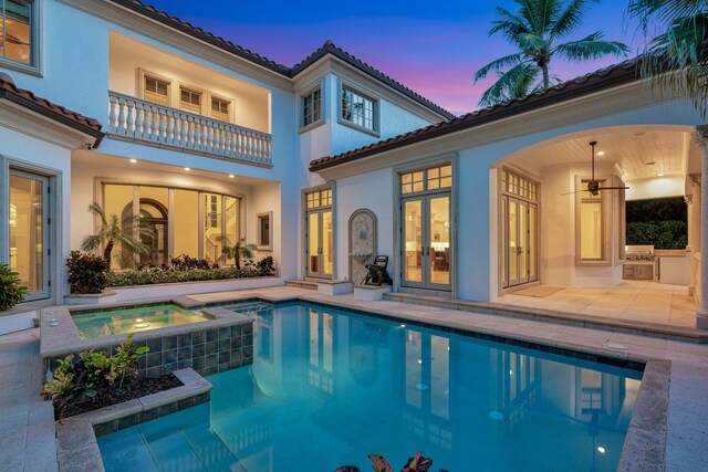 pool at dusk with a patio area and an in ground hot tub