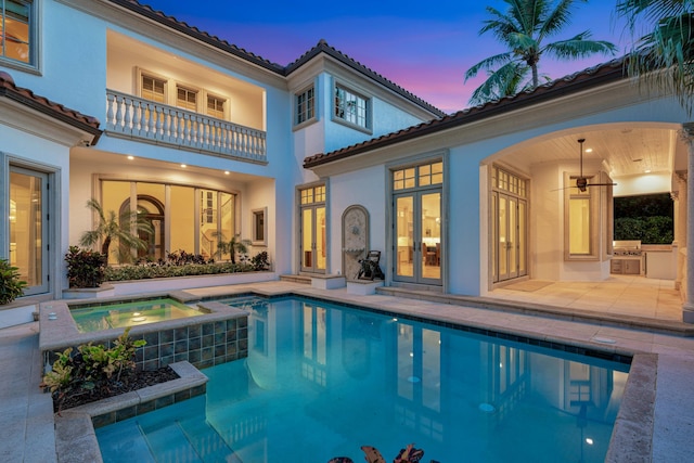 back of property at dusk featuring french doors, a tiled roof, stucco siding, an outdoor kitchen, and a balcony