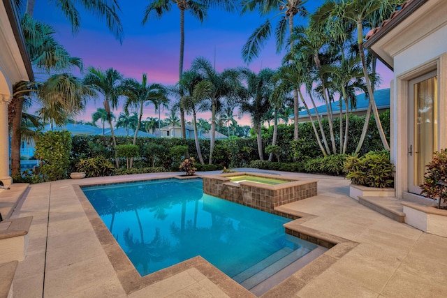pool at dusk featuring a patio area and a pool with connected hot tub