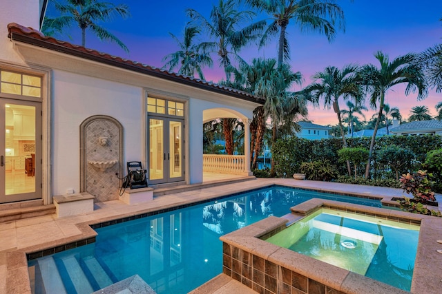 pool at dusk featuring an in ground hot tub, french doors, and a patio