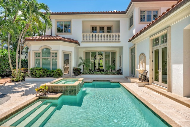 back of property with a balcony, a patio, and a pool with hot tub