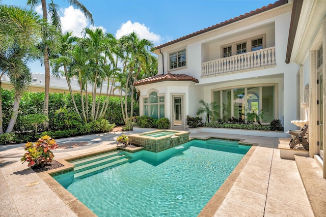back of property with stucco siding, a pool with connected hot tub, a tile roof, a balcony, and a patio area