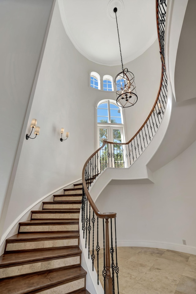 stairs with crown molding, an inviting chandelier, a high ceiling, and tile patterned flooring