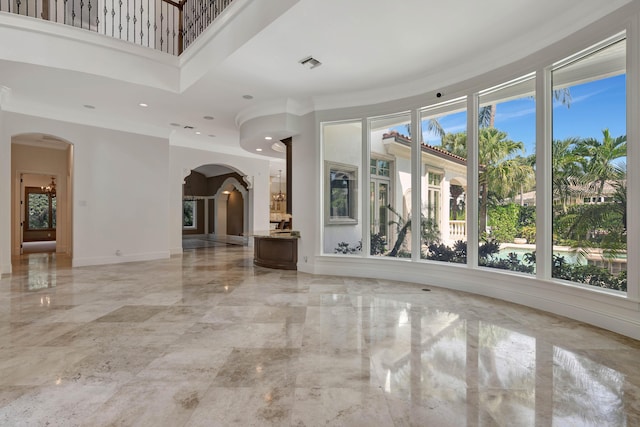 unfurnished living room with a wealth of natural light, visible vents, marble finish floor, and arched walkways