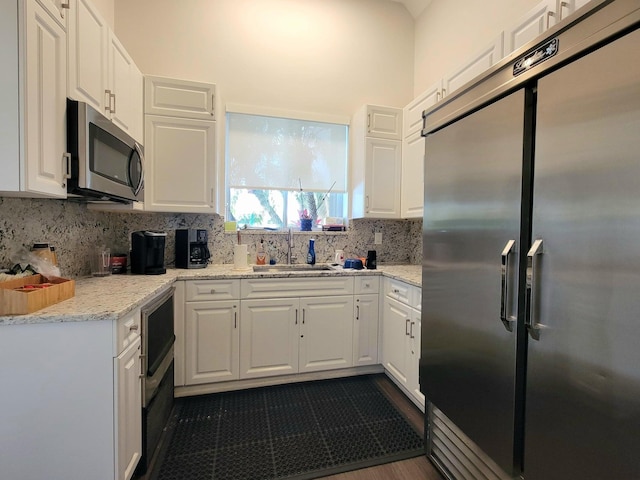 kitchen featuring backsplash, white cabinets, appliances with stainless steel finishes, light stone counters, and sink