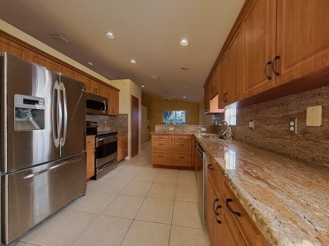 kitchen featuring backsplash, appliances with stainless steel finishes, light stone counters, sink, and light tile patterned flooring