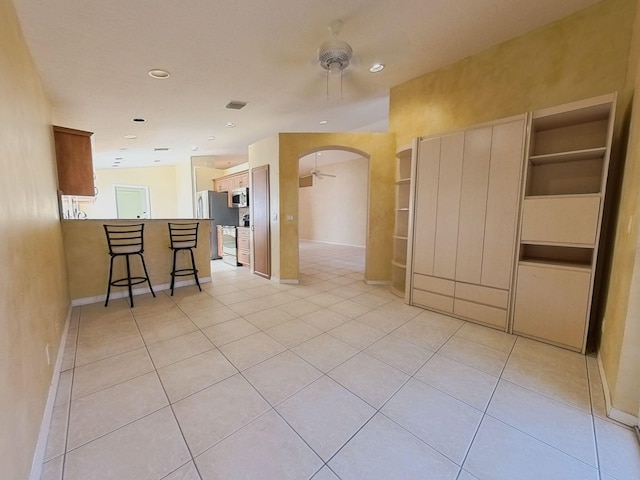 interior space featuring a kitchen breakfast bar, appliances with stainless steel finishes, ceiling fan, and light tile patterned floors