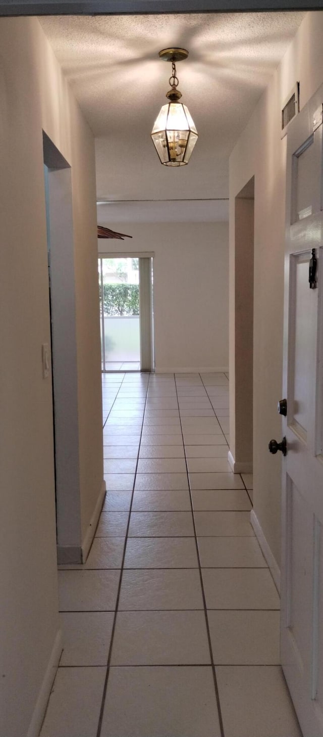 hallway with a textured ceiling and light tile patterned floors