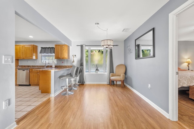 kitchen featuring a breakfast bar, light hardwood / wood-style floors, stainless steel dishwasher, hanging light fixtures, and kitchen peninsula