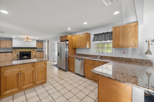 kitchen featuring appliances with stainless steel finishes, sink, a fireplace, kitchen peninsula, and light tile patterned flooring